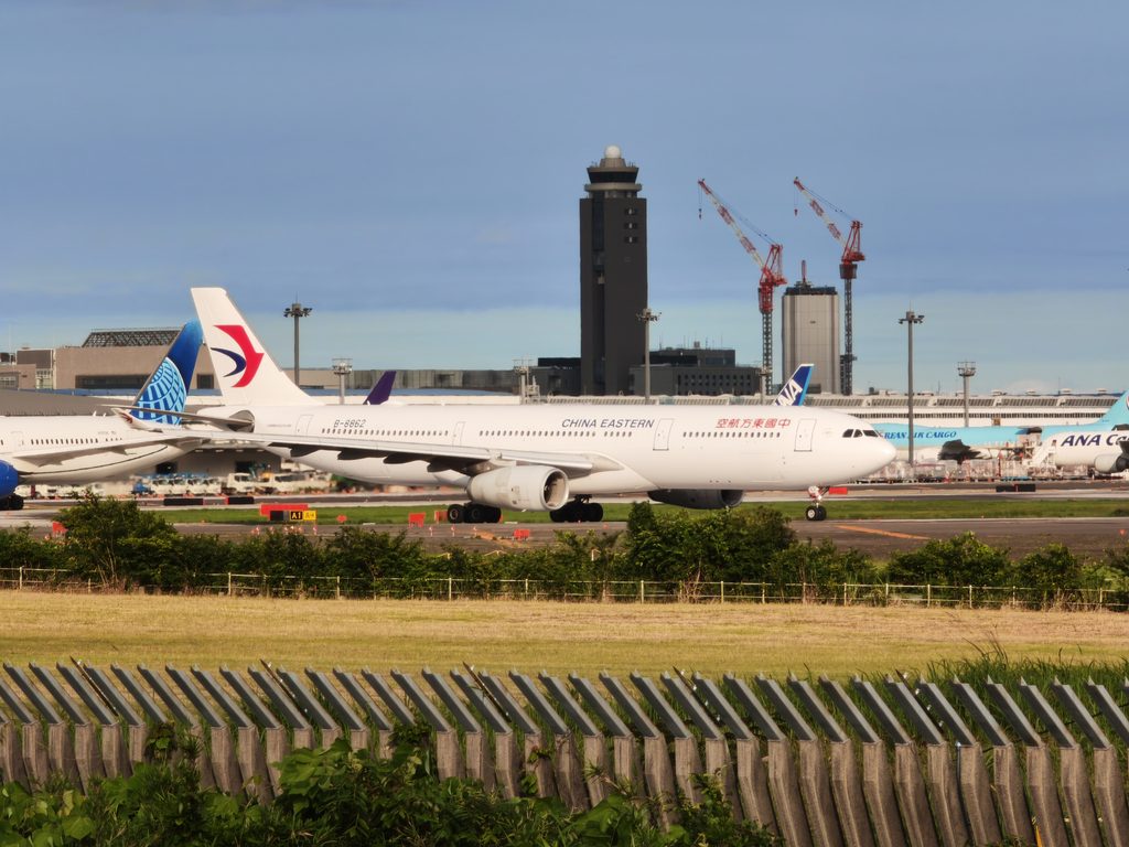 成田空港の滑走路付近をタキシング（地上移動）する中国東方航空の白い機体。さくらの山公園から撮影